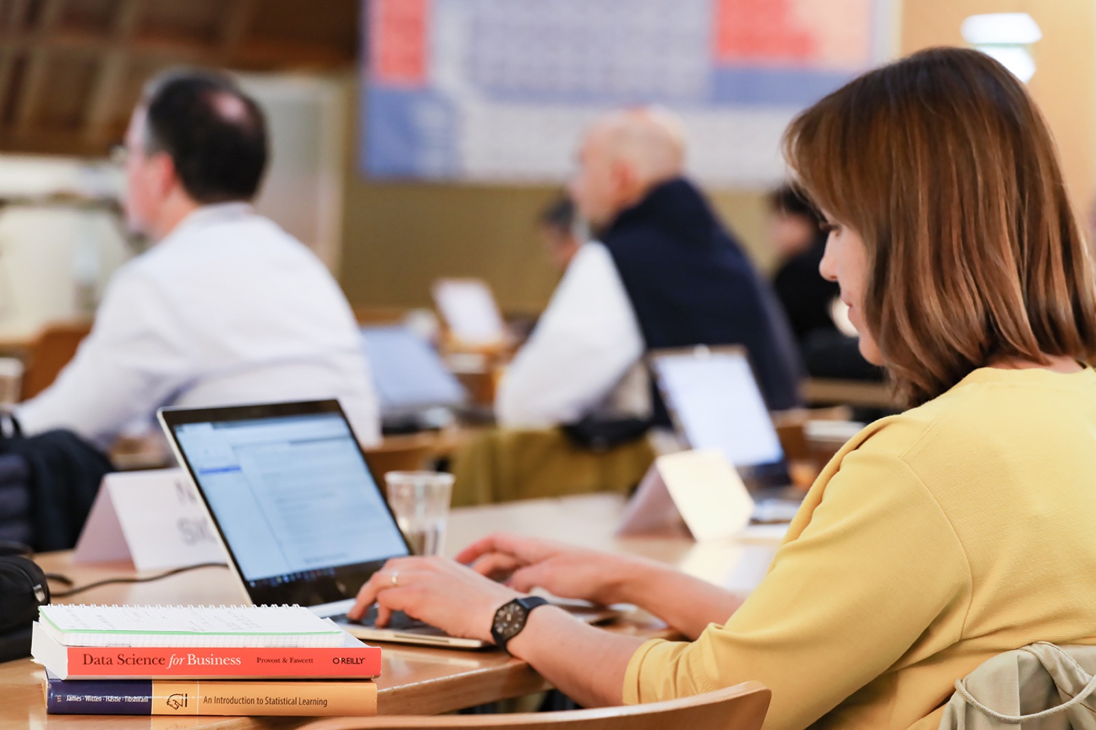 Participants working on laptops during the Data Science for Managers program - a Data Science for Business textbook in the foreground